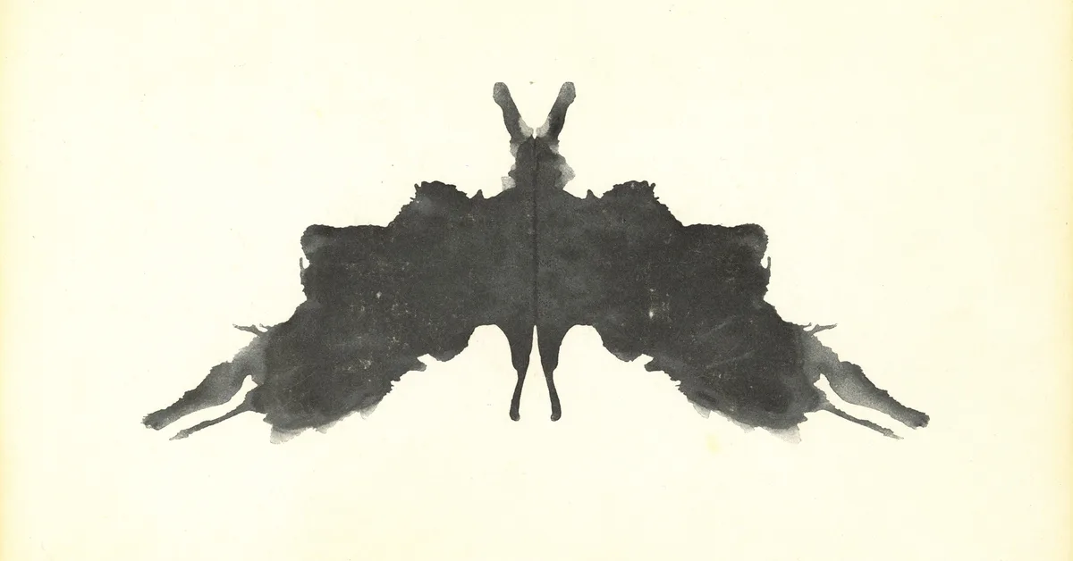 A symmetrical black inkblot with pointed wings on a cream card